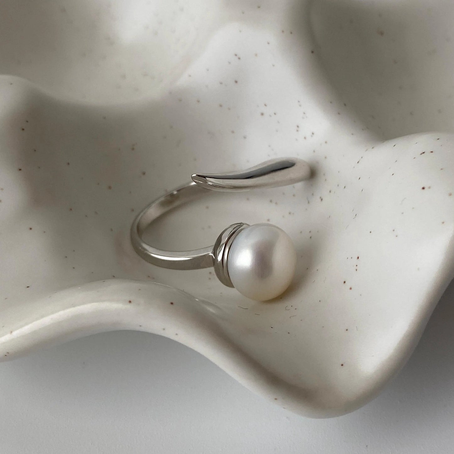 derMomentø - Handcrafted large pearl open ring with a naturally grown freshwater baroque pearl, set on a white rhodium-plated silver band. Display on a ceramic tray on a clean background.