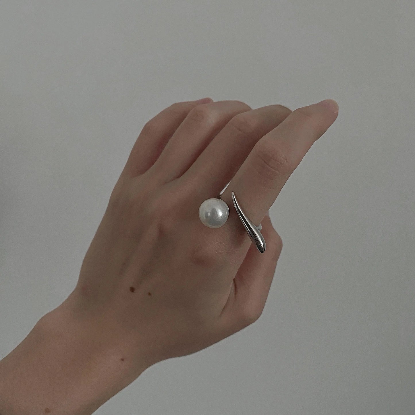 derMomentø - Handcrafted large pearl open ring with a naturally grown freshwater baroque pearl, set on a white rhodium-plated silver band. Display on hand on a clean background.