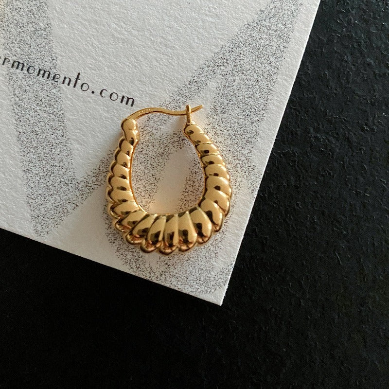 A single bold hoop earrings feature a unique twisted design with dermomento.com at background.
