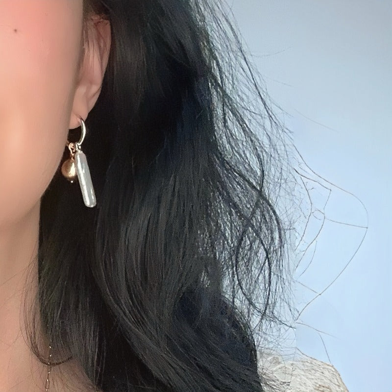 The Golden Ball & Pearl Charm Hoop Earrings feature a drop baroque pearl and a 14KGF golden ball charm suspended from mini sterling silver hoops. These versatile hoops can be worn solo or with any drop and charm to suit your style.