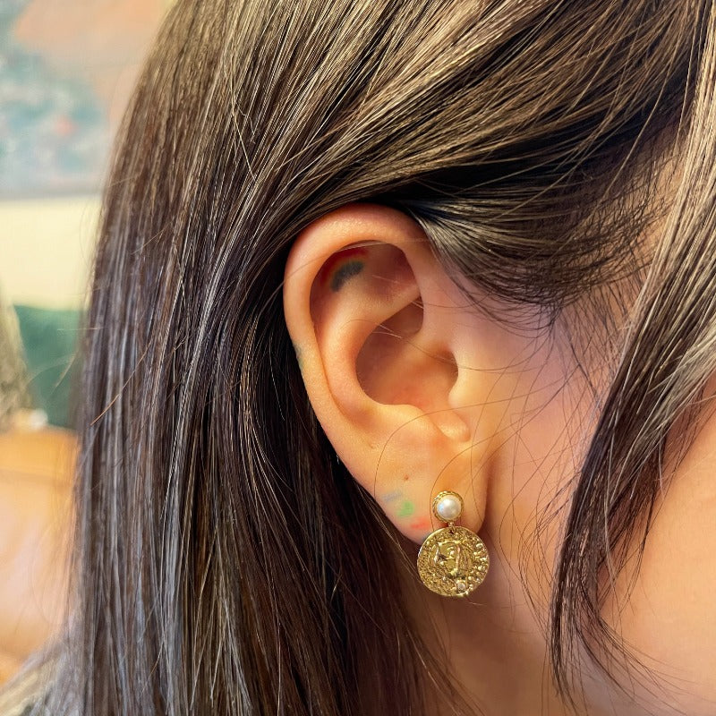 Model wearing the Alwina Drop Stud Earrings - a mini pearl design (non-natural pearl) enveloped in 18K gold vermeil silver and accented by tiny zircons and intricate tin relief detailing on each round tile.