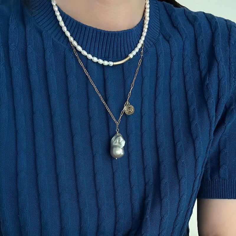 The Charlotte Baroque Pearl Necklace features a stunning natural blue-grey baroque pearl, elegantly hanging from a 14K Gold-Filled chain and embellished with charming gold coin accents.