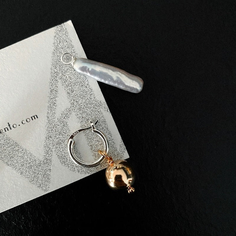 The Golden Ball & Pearl Charm Hoop Earrings feature a drop baroque pearl and a 14KGF golden ball charm suspended from mini sterling silver hoops. These versatile hoops can be worn solo or with any drop and charm to suit your style.