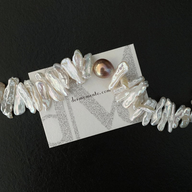 Close up of a cream pearl choker necklace with a uniquely coloured baroque pearl at its centre with dermomento.com at background.