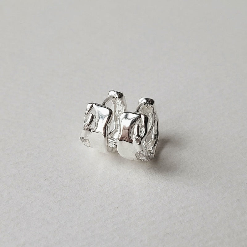 The Elfi Hoop Earrings crafted from sterling silver, have a unique texture with uneven cutouts and small cubic zirconia embellishments.