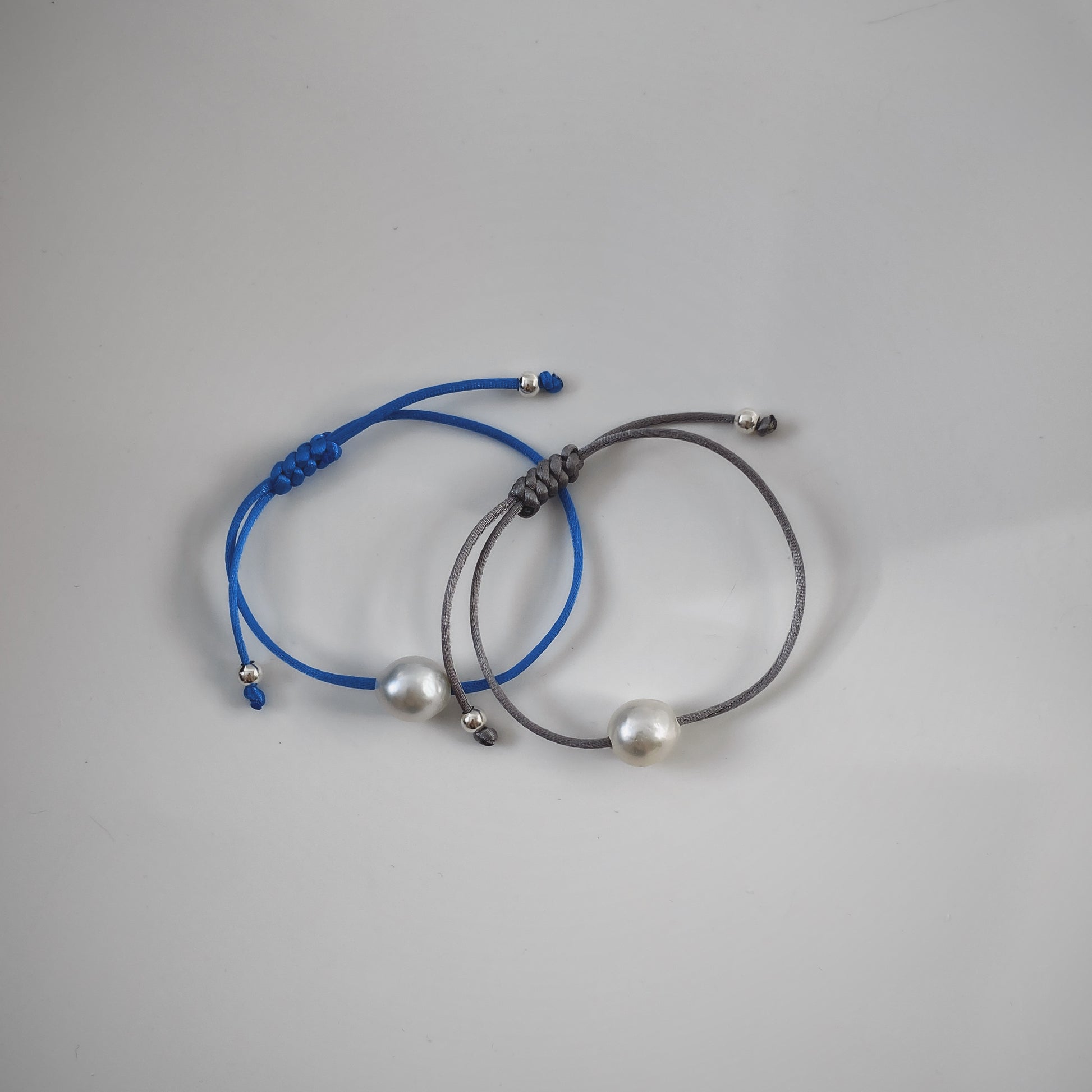 2 pieces of handmade single pearl silk cord string bracelets featuring a single natural baroque oval pearl with a stunning silver-blue lustre , delicately strung on adjustable silk cord in blue and grey and adorned with silver beads.