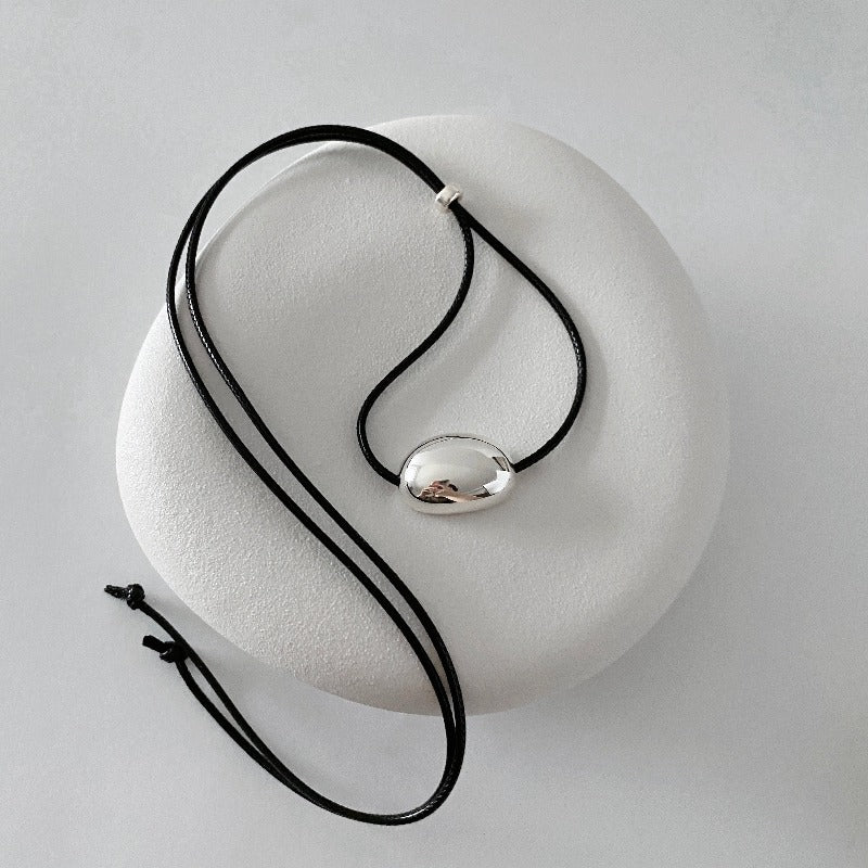 derMomentø - Minimalist Black Cord Necklace with Silver Bean Pendant, made with a black leather string cord and featuring a bold chunky bean pendant in sterling silver.