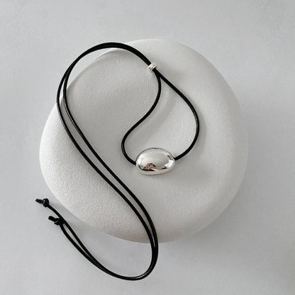 derMomentø - Minimalist Black Cord Necklace with Silver Bean Pendant, made with a black leather string cord and featuring a bold chunky bean pendant in sterling silver.