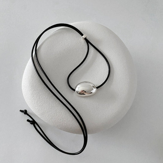 derMomentø - Minimalist Black Cord Necklace with Silver Bean Pendant, made with a black leather string cord and featuring a bold chunky bean pendant in sterling silver.