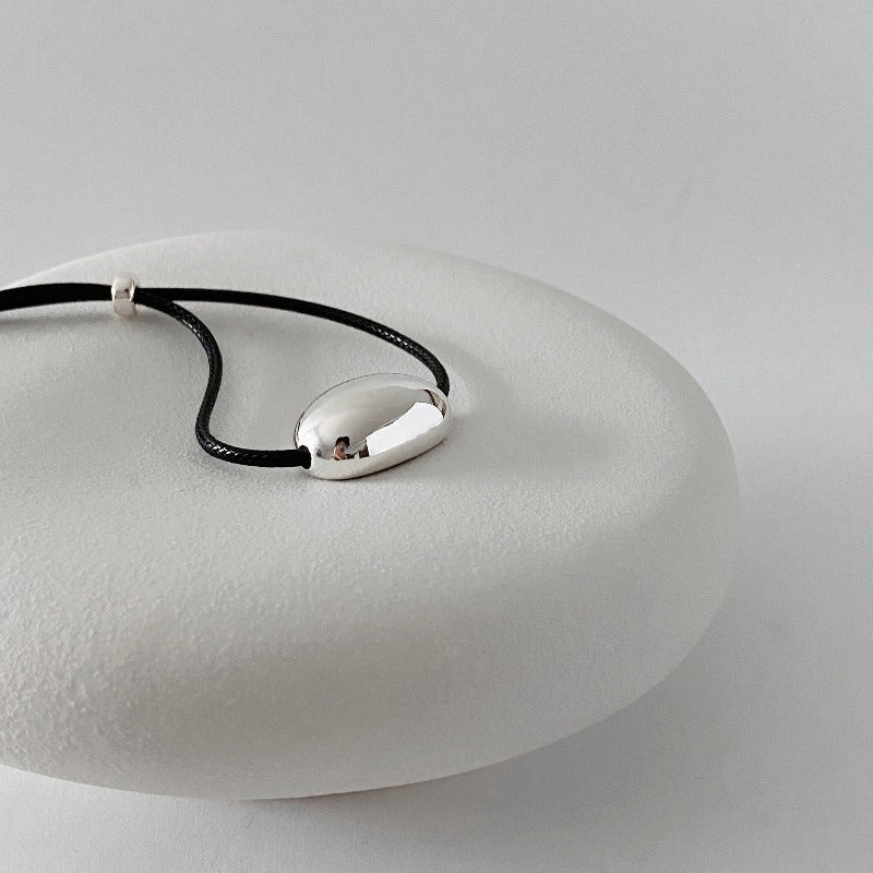 derMomentø - Minimalist Black Cord Necklace with Silver Bean Pendant, made with a black leather string cord and featuring a bold chunky bean pendant in sterling silver.