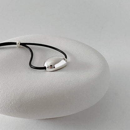 derMomentø - Minimalist Black Cord Necklace with Silver Bean Pendant, made with a black leather string cord and featuring a bold chunky bean pendant in sterling silver.