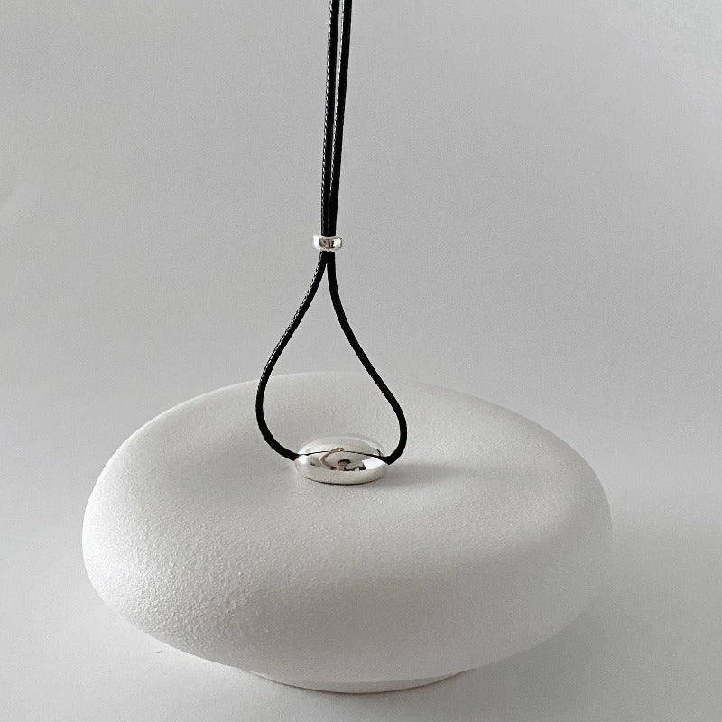 derMomentø - Minimalist Black Cord Necklace with Silver Bean Pendant, made with a black leather string cord and featuring a bold chunky bean pendant in sterling silver.