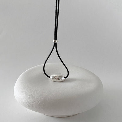 derMomentø - Minimalist Black Cord Necklace with Silver Bean Pendant, made with a black leather string cord and featuring a bold chunky bean pendant in sterling silver.