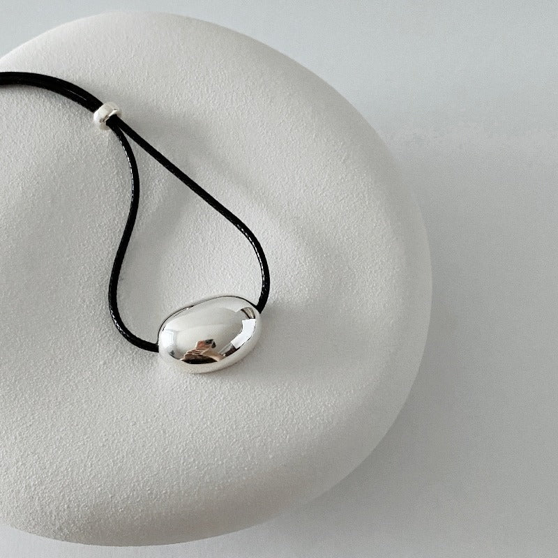 derMomentø - Minimalist Black Cord Necklace with Silver Bean Pendant, made with a black leather string cord and featuring a bold chunky bean pendant in sterling silver.