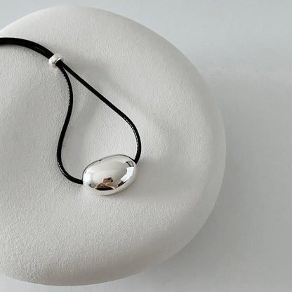 derMomentø - Minimalist Black Cord Necklace with Silver Bean Pendant, made with a black leather string cord and featuring a bold chunky bean pendant in sterling silver.
