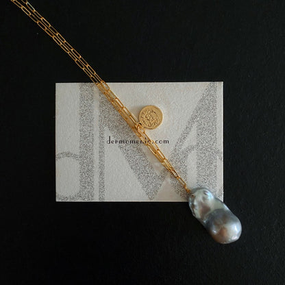 The Charlotte Baroque Pearl Necklace features a stunning natural blue-grey baroque pearl, elegantly hanging from a 14K Gold-Filled chain and embellished with charming gold coin accents.
