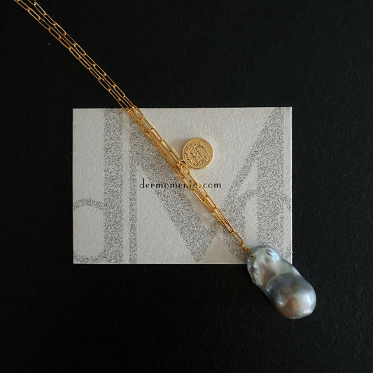 The Charlotte Baroque Pearl Necklace features a stunning natural blue-grey baroque pearl, elegantly hanging from a 14K Gold-Filled chain and embellished with charming gold coin accents.