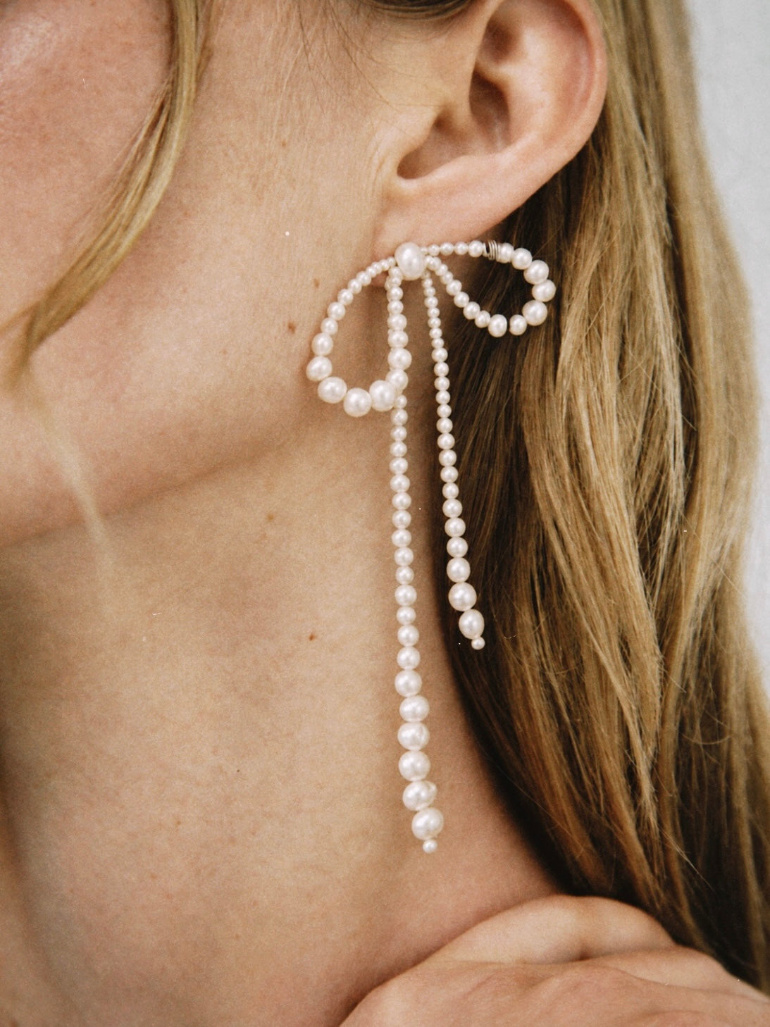 Oversized COLETTE pearl bow earrings worn on ear