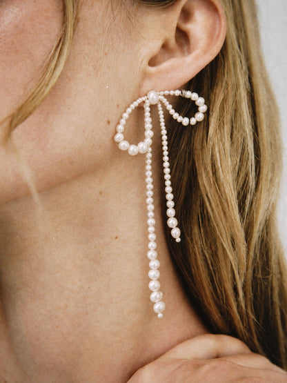 Oversized COLETTE pearl bow earrings worn on ear