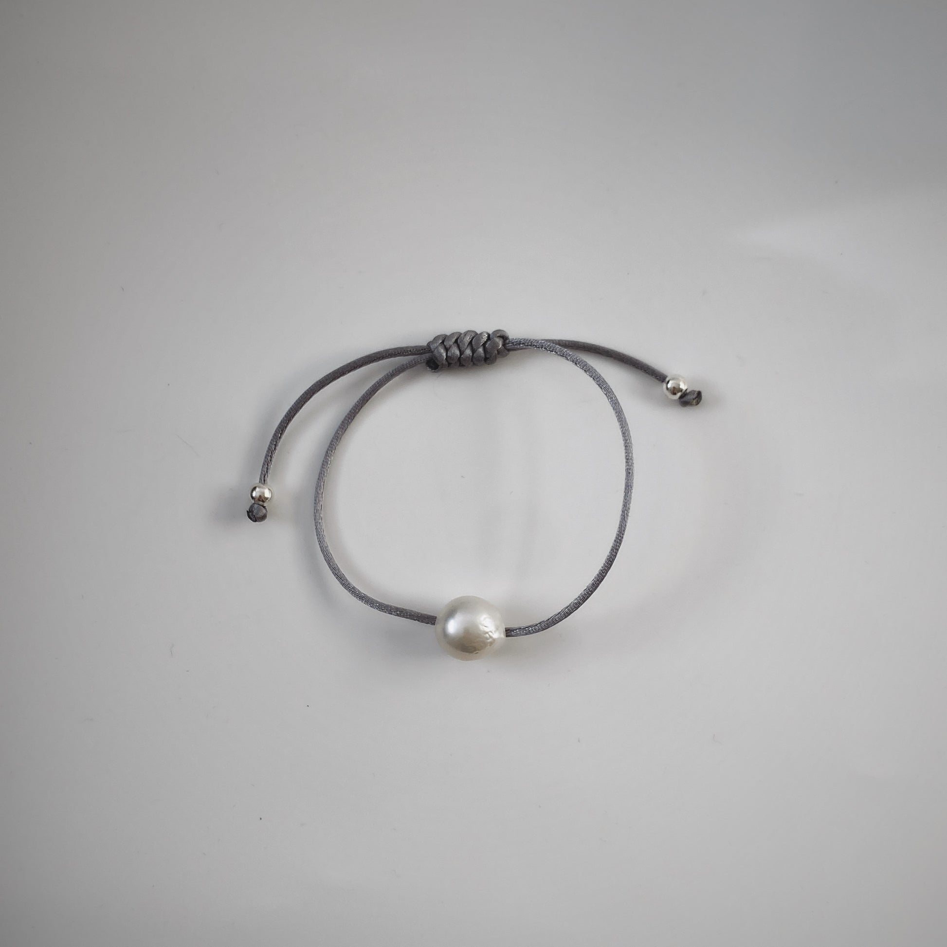 Handmade single pearl silk cord string bracelets featuring a single natural baroque oval pearl with a stunning silver-blue lustre , delicately strung on adjustable gray silk cord and adorned with silver beads.