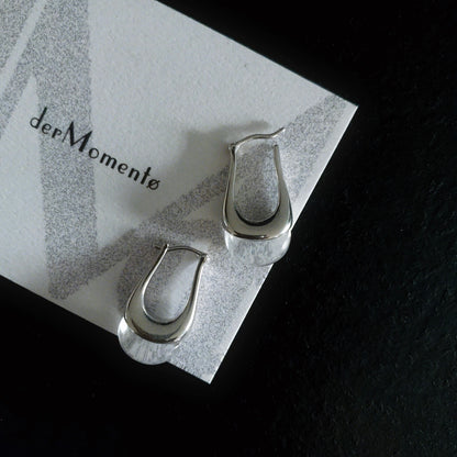 Close-up of bold silver hoop earrings with natural crystal quartz gemstones, displayed on brand card with name derMomentø, on a black background.