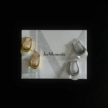 Chunky silver and gold hoop earrings with natural green prehnite and clear quartz gemstones, modern minimalist jewelry design. Displayed on a brand card with name derMomentø, on a black background.