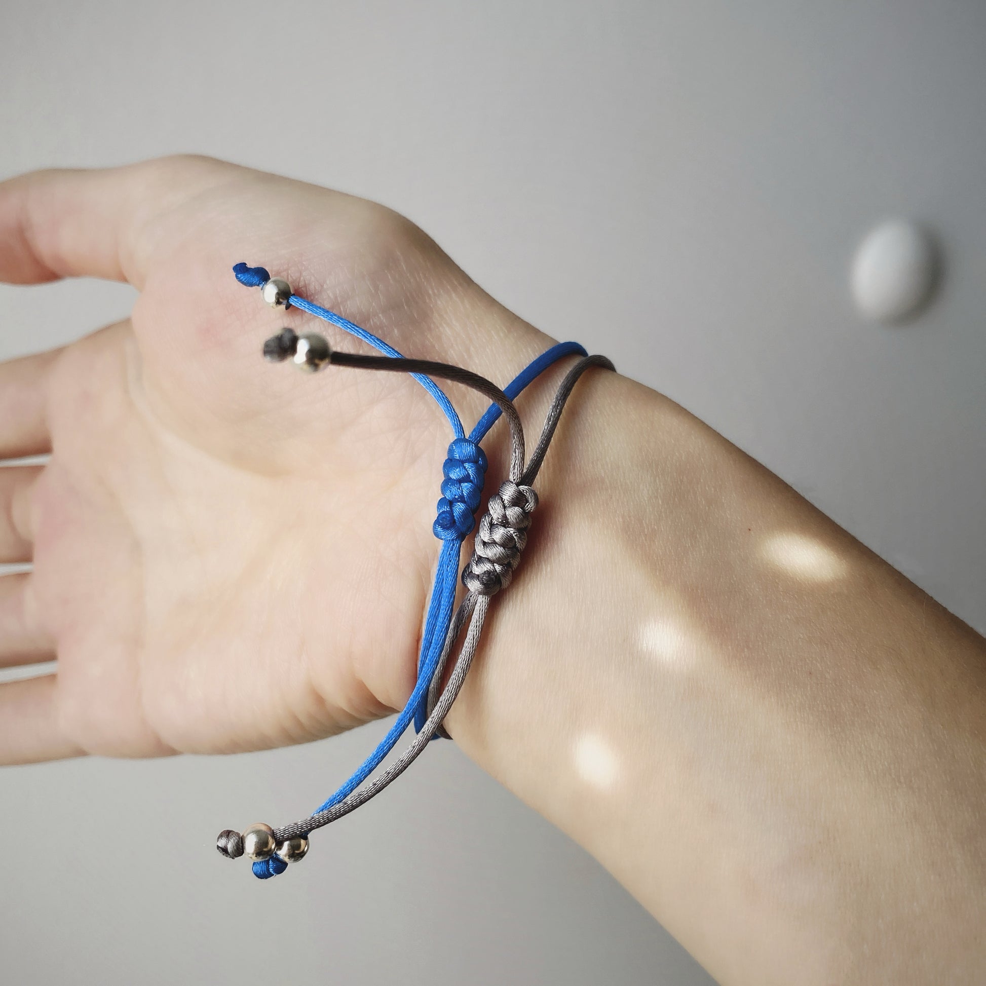 Close up of 2 pieces of handmade single pearl silk cord string bracelets featuring a single natural baroque oval pearl with a stunning silver-blue lustre , delicately strung on adjustable silk cord in blue and grey and adorned with silver beads.