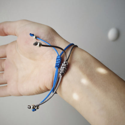 Close up of 2 pieces of handmade single pearl silk cord string bracelets featuring a single natural baroque oval pearl with a stunning silver-blue lustre , delicately strung on adjustable silk cord in blue and grey and adorned with silver beads.