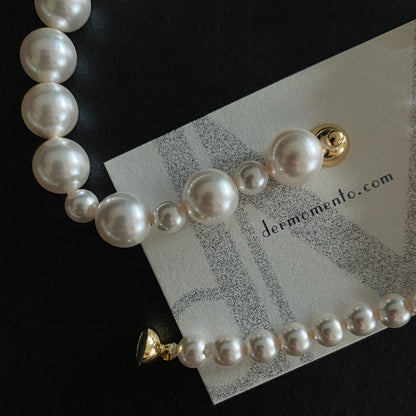 A close up of Mira Crystal Pearl Necklace with its golden magnetic clasp. Brand website "dermomento.com" at background.