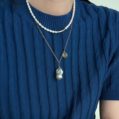 The Charlotte Baroque Pearl Necklace features a stunning natural blue-grey baroque pearl, elegantly hanging from a 14K Gold-Filled chain and embellished with charming gold coin accents.
