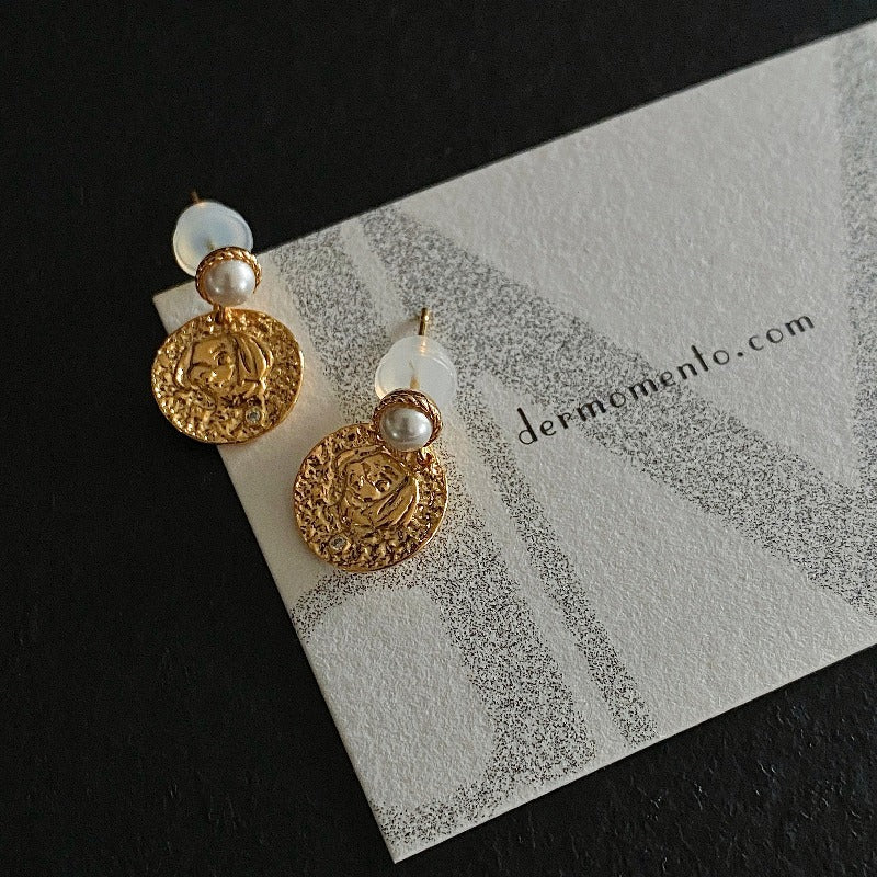 The Alwina Drop Stud Earrings - a mini pearl design (non-natural pearl) expertly enveloped in 18K gold vermeil silver and accented by tiny zircons and intricate tin relief detailing on each round tile. With dermomento.com at background.