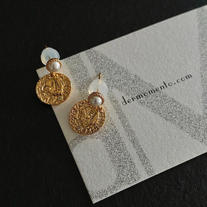 The Alwina Drop Stud Earrings - a mini pearl design (non-natural pearl) expertly enveloped in 18K gold vermeil silver and accented by tiny zircons and intricate tin relief detailing on each round tile. With dermomento.com at background.