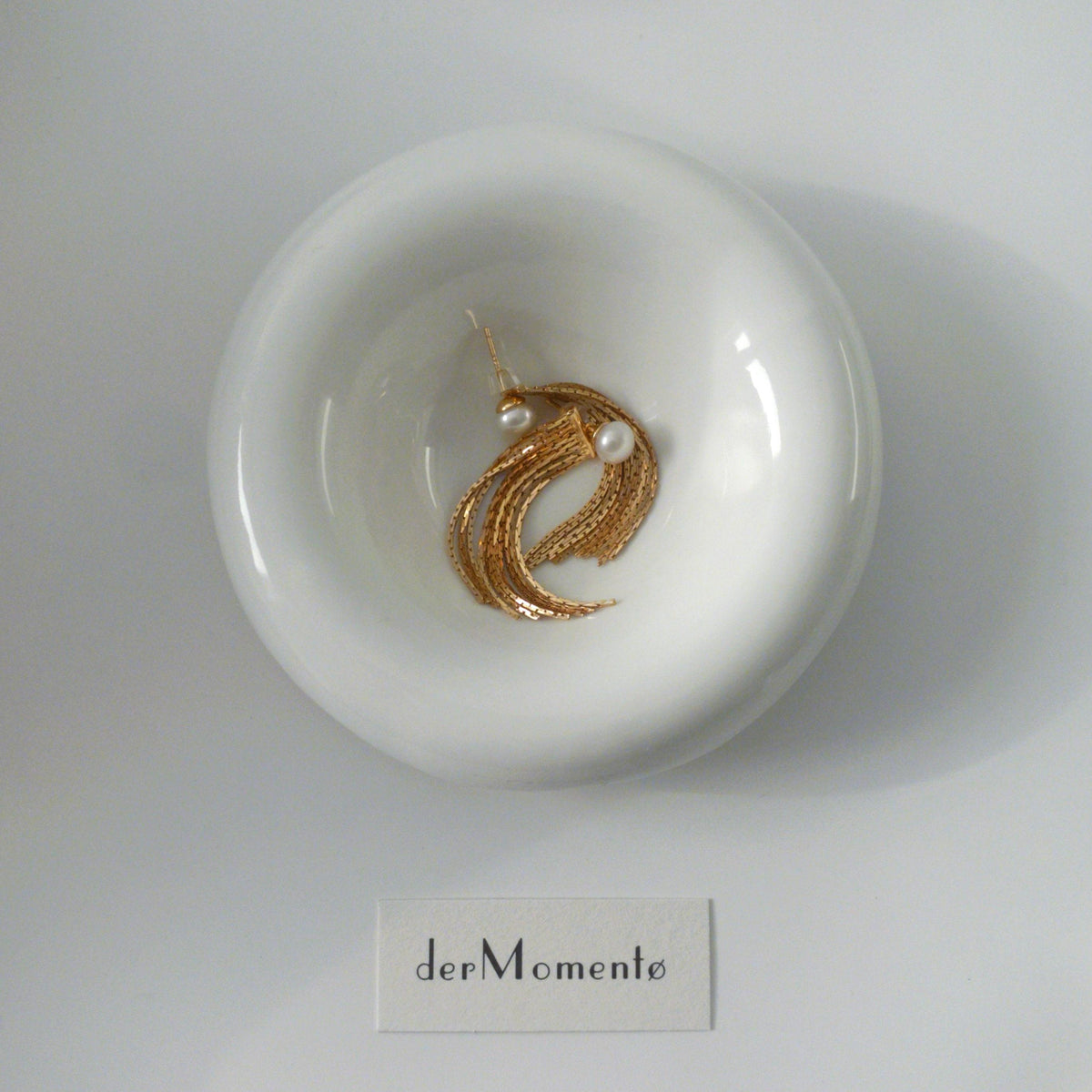 THEA gold vermeil pearl tassel earrings arranged on a white ceramic dish