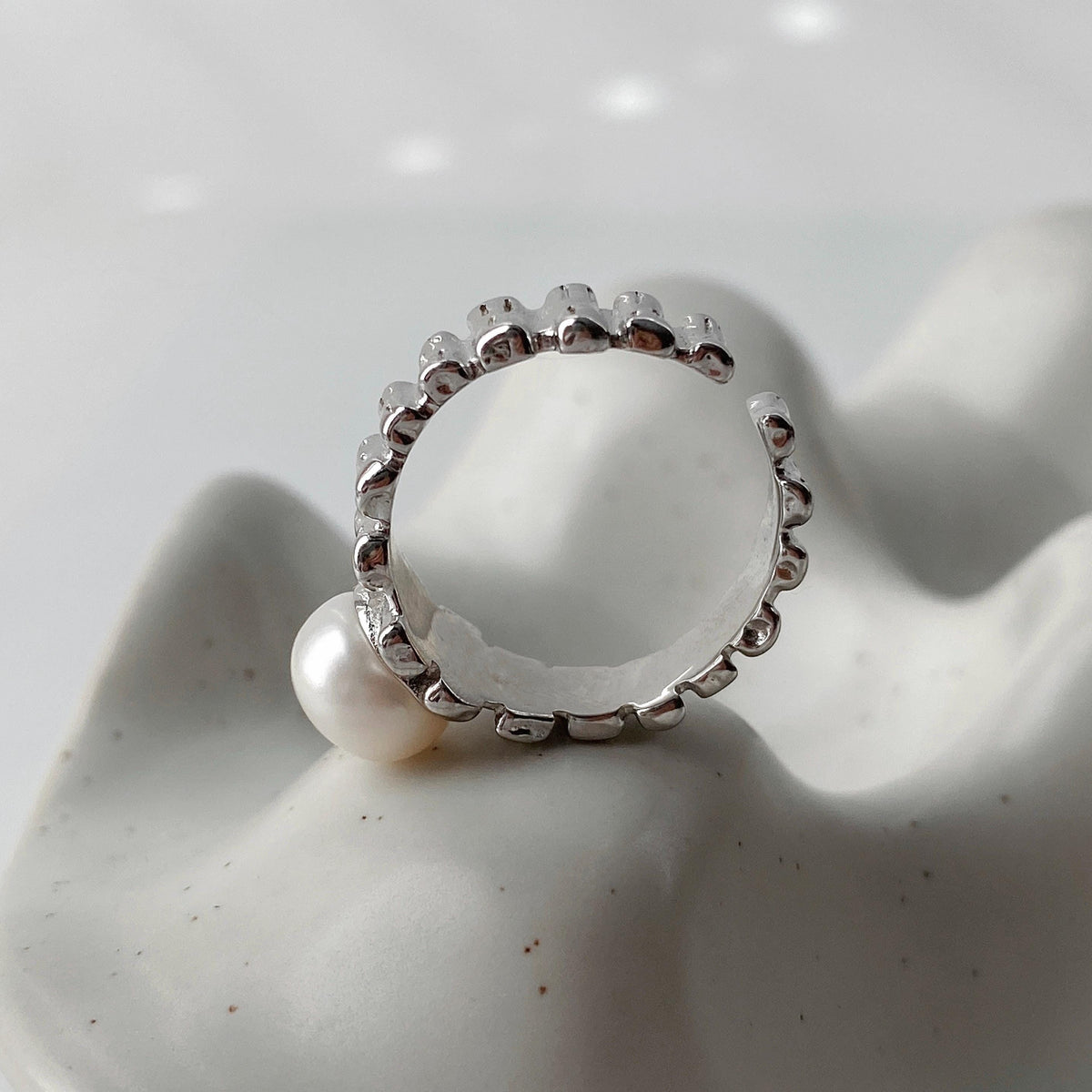 Close-up of the side view of irregular textured silver surface and freshwater pearl